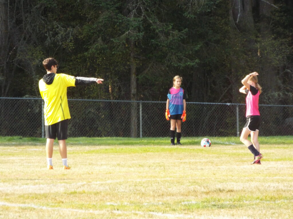 A referee pointing towards a ball as two soccer players are standing on the field.